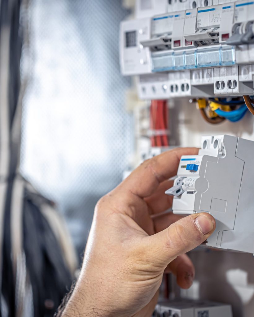 A male electrician works in a switchboard with an electrical connecting cable. Male electrician at the checkout counter on a blurred background of a switchboard.
